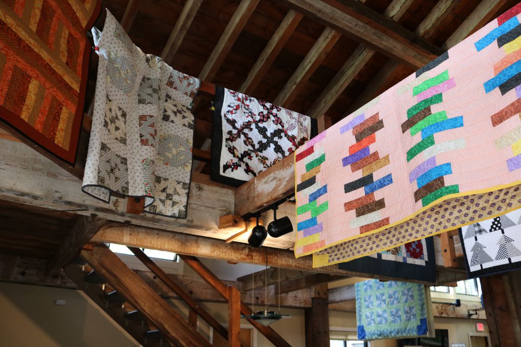 Quilts hanging over a railing and rafters